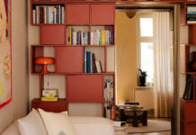 Μια κόκκινη βιβλιοθήκη σπάει την κυριαρχία του μπεζ σ’ αυτό το σαλόνι